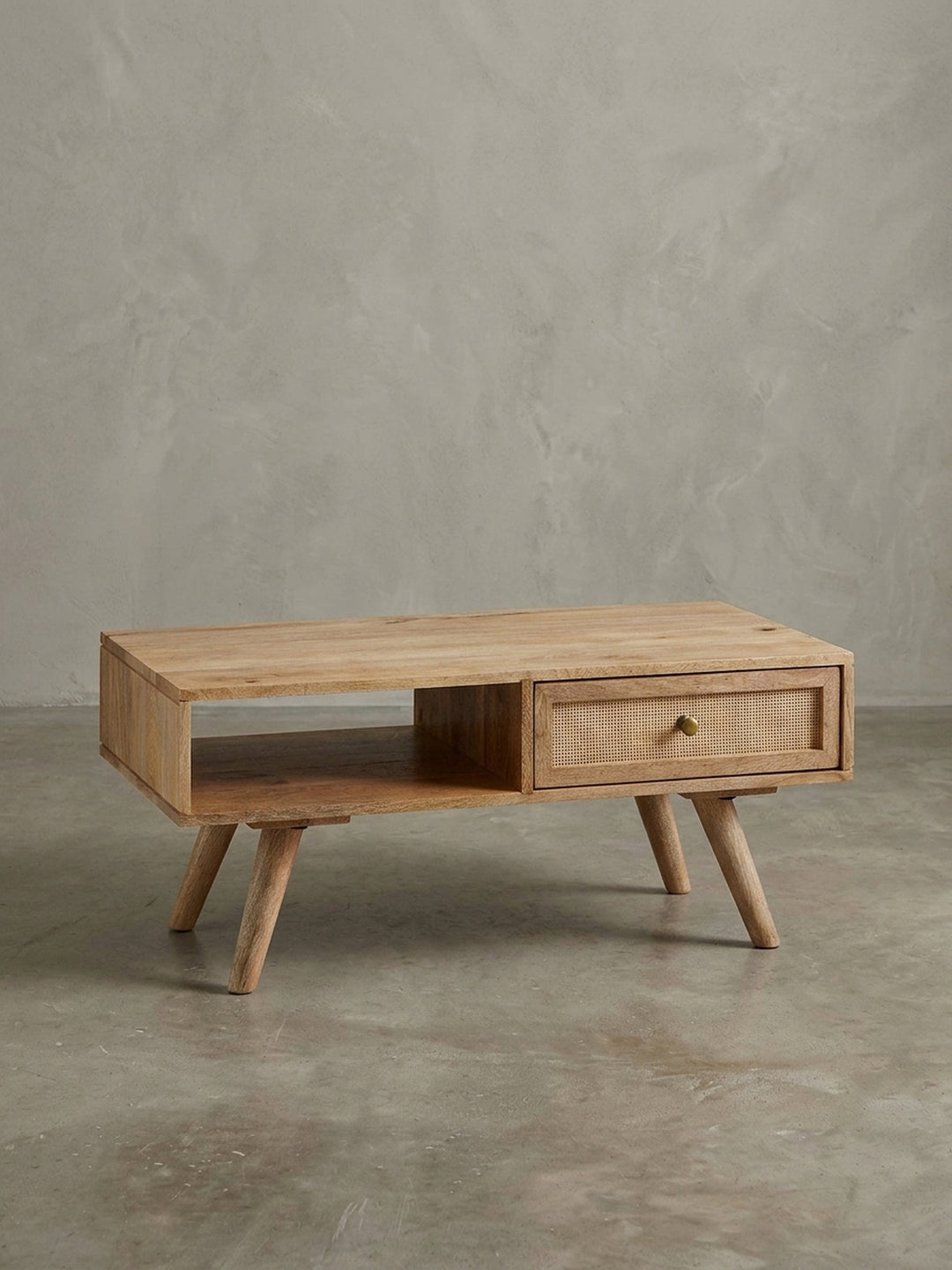 Design-Couchtisch in 3/4-Ansicht, der die asymmetrische Anordnung von Schublade mit Rattan und offenem Staufach aus massivem Mangoholz hervorhebt._