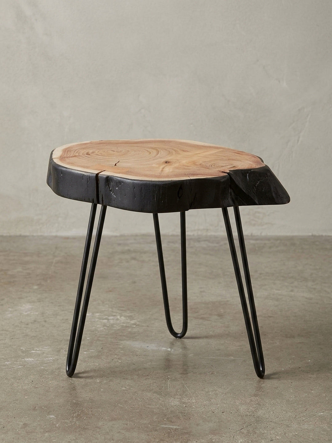 Gesamtansicht des Design-Beistelltisches, der die harmonische Verbindung von warmem Akazienholz mit der rohen, schwarzen Baumkante und filigranen Metallbeinen zeigt._