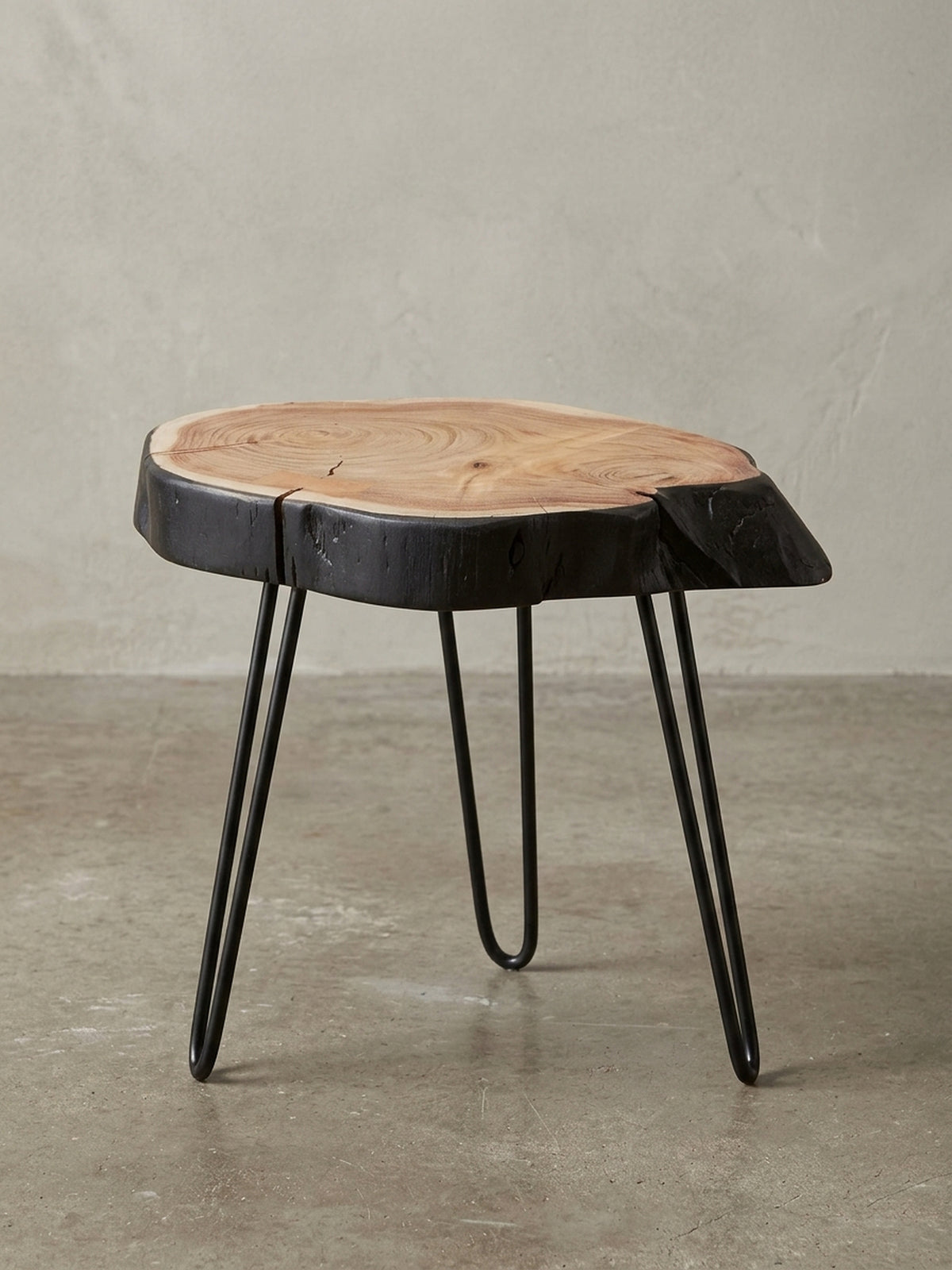 Gesamtansicht des Design-Beistelltisches, der die harmonische Verbindung von warmem Akazienholz mit der rohen, schwarzen Baumkante und filigranen Metallbeinen zeigt.