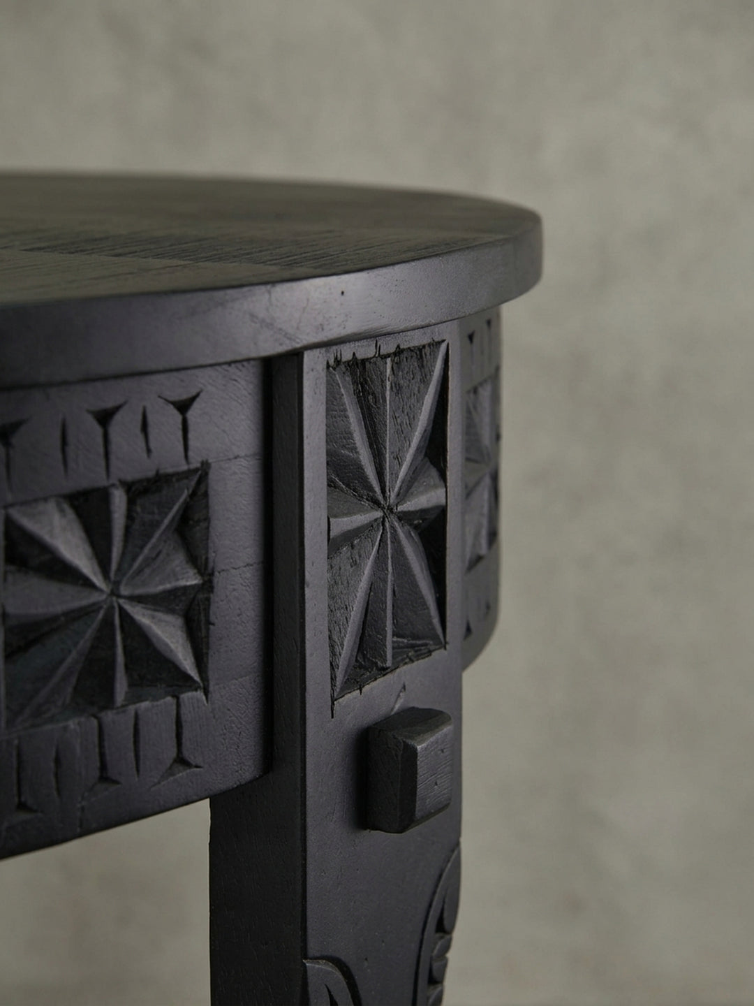 Nahaufnahme der Sternschnitzerei auf der Zarge des runden Sofatischs, ein charakteristisches Detail des orientalischen Designs aus schwarz lackiertem Massivholz._