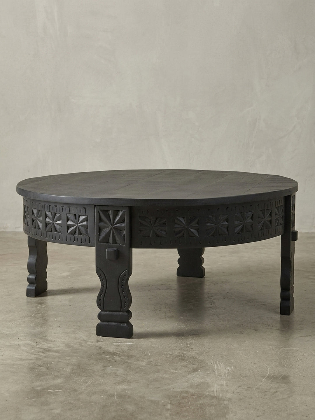 Dreiviertelansicht des massiven runden Sofatischs, der die kunstvollen orientalischen Schnitzereien an der Zarge und den robusten Beinen aus schwarzem Mangoholz detailreich zeigt._