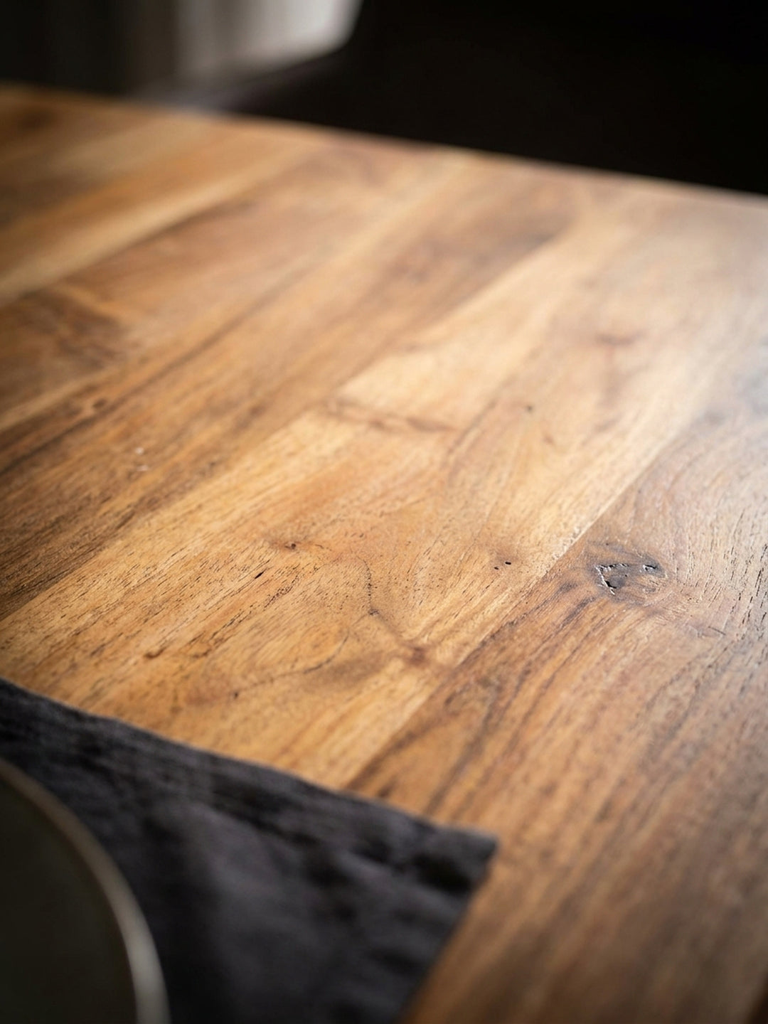 Nahaufnahme der lebendigen Maserung und der natürlichen Baumkante des massiven Akazienholz-Esstisches, die warme Holzstruktur im Detail._