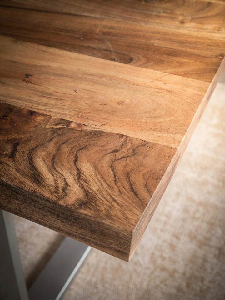 Detailaufnahme der lebendigen Maserung des Akazie Massivholztisches, die warme Holzoberfläche mit einzigartiger Baumkante und lackiertem Finish im Nahfokus._