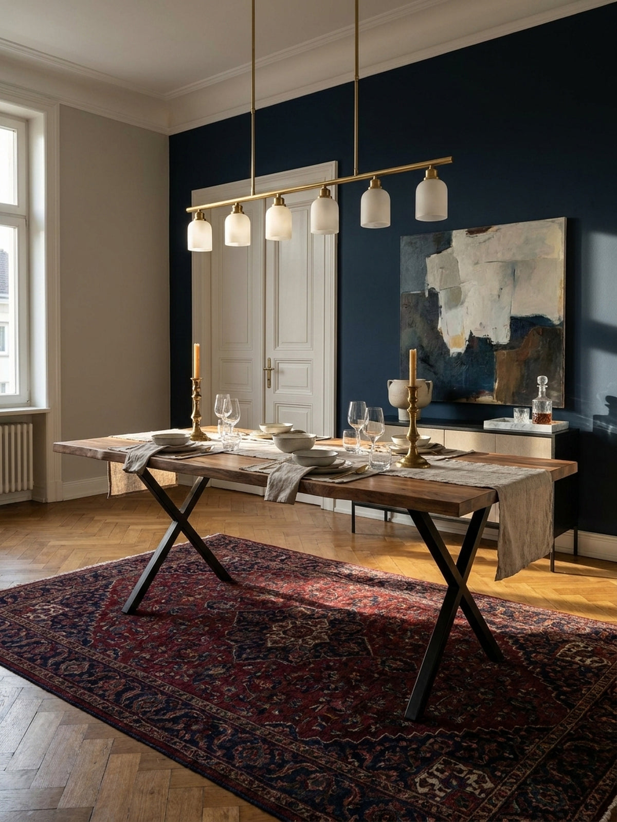 Ein großer Esstisch aus massivem Akazienholz mit schwarzen X-Beinen als Mittelpunkt eines eleganten Esszimmers mit Fischgrätparkett und Samtstühlen._