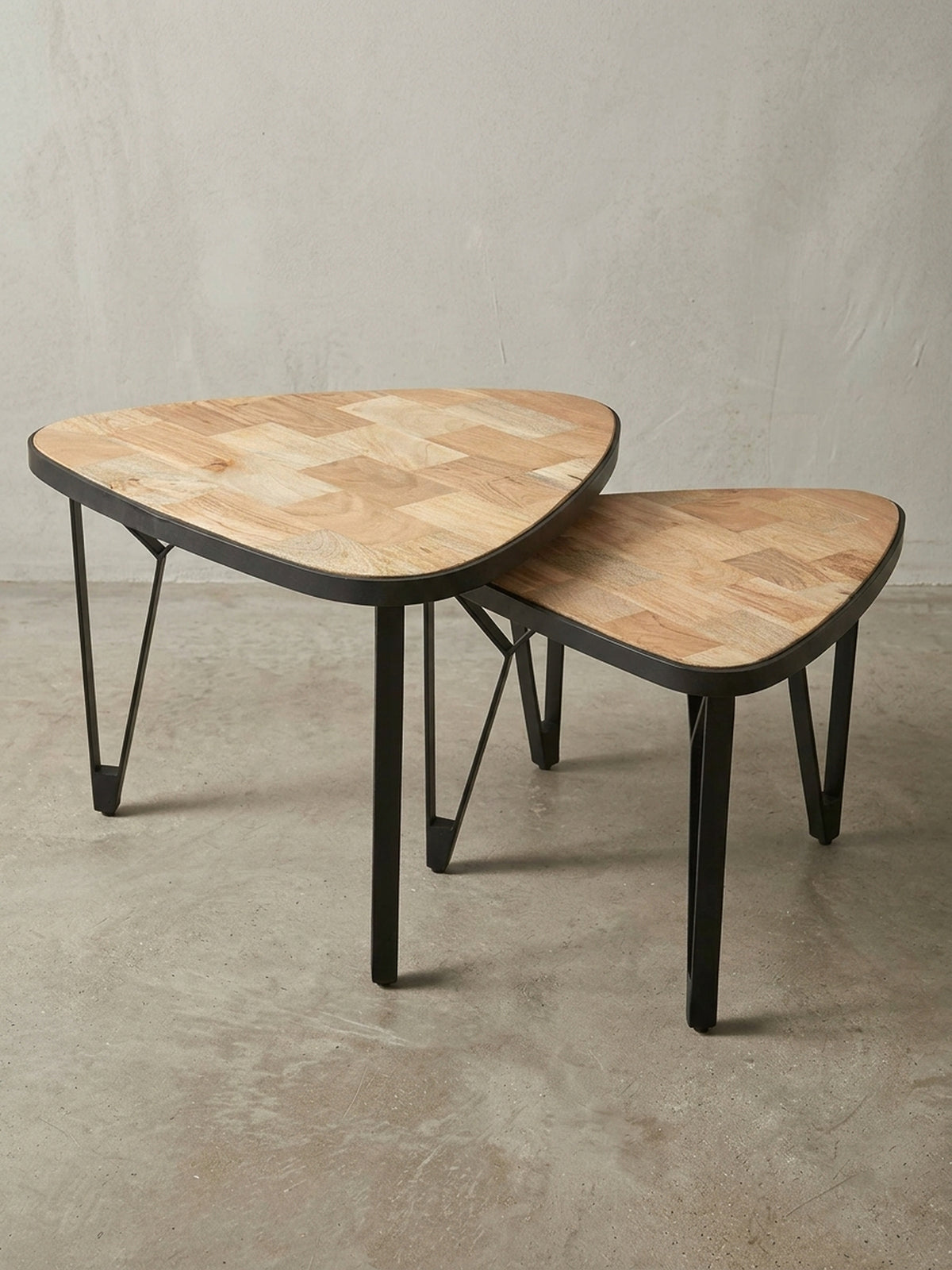 Design Couchtisch Set aus massivem Holz mit schwarzem Metallgestell, die zwei dreieckigen Tische sind auf weißem Hintergrund ineinander geschachtelt dargestellt._