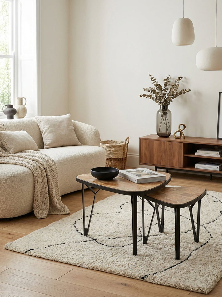 Ein Set aus zwei dreieckigen Couchtischen aus Mango-Massivholz steht auf einem Wollteppich in einem eleganten Wohnzimmer, stilvoll neben einem Sofa arrangiert._