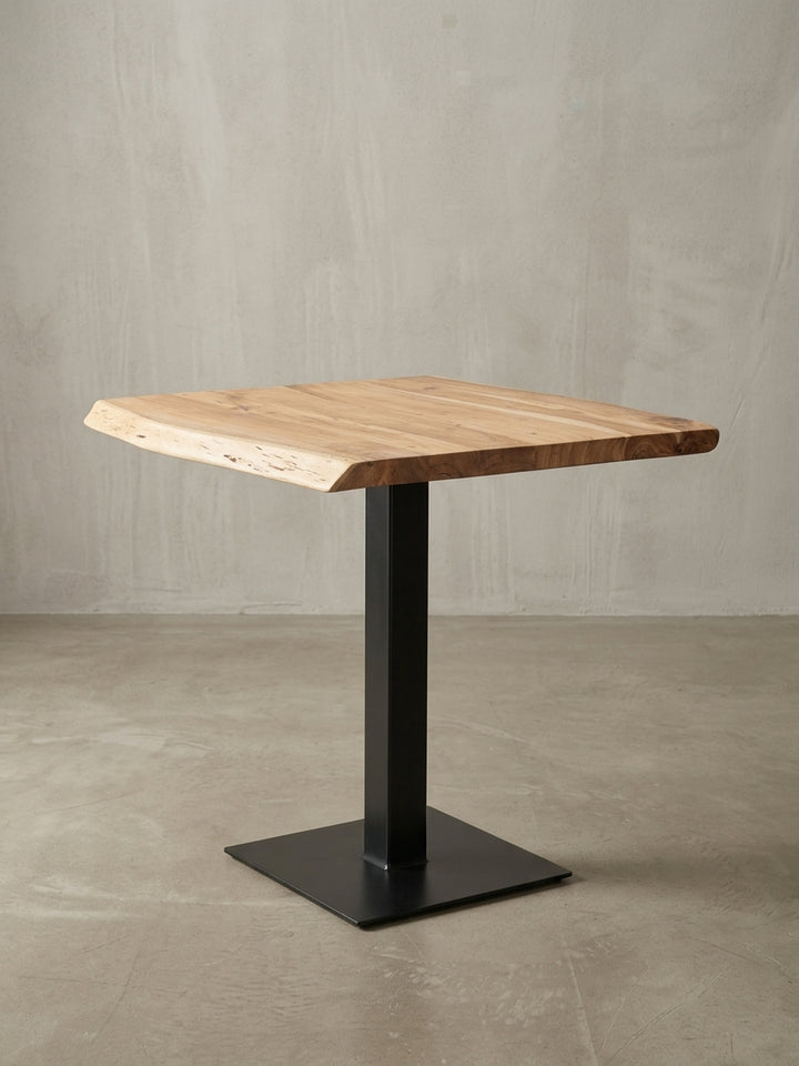 Design-Küchentisch aus Akazie in einer 3/4-Ansicht, die die einzigartige Baumkante und den Kontrast zwischen der Holzplatte und dem mattschwarzen Edelstahlgestell zeigt._