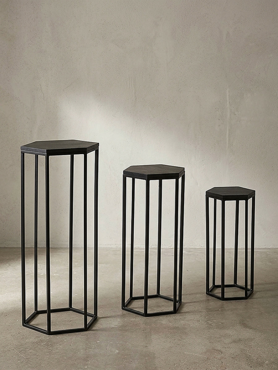 Dreiteiliges Satztisch Set aus schwarzem Holz und Metall in sechseckiger Säulenform frontal freigestellt vor weißem Hintergrund._