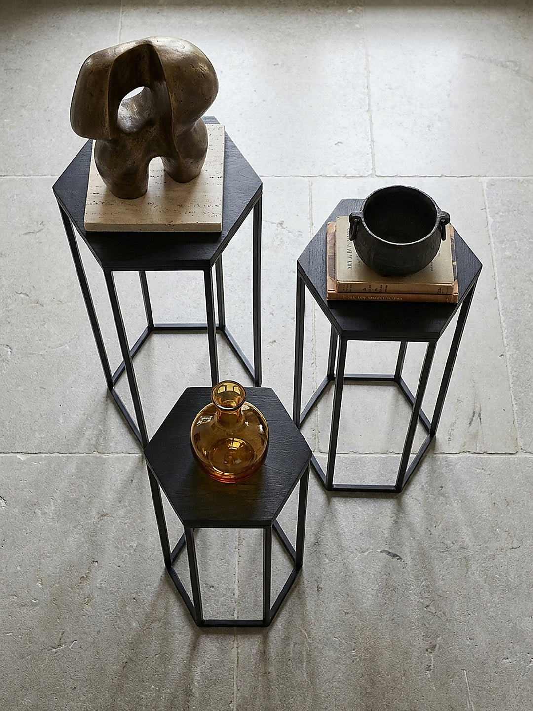 Draufsicht auf das dreiteilige Beistelltisch Set mit sechseckiger Form im modernen Galerieraum neben einer abstrakten Bronzeskulptur._