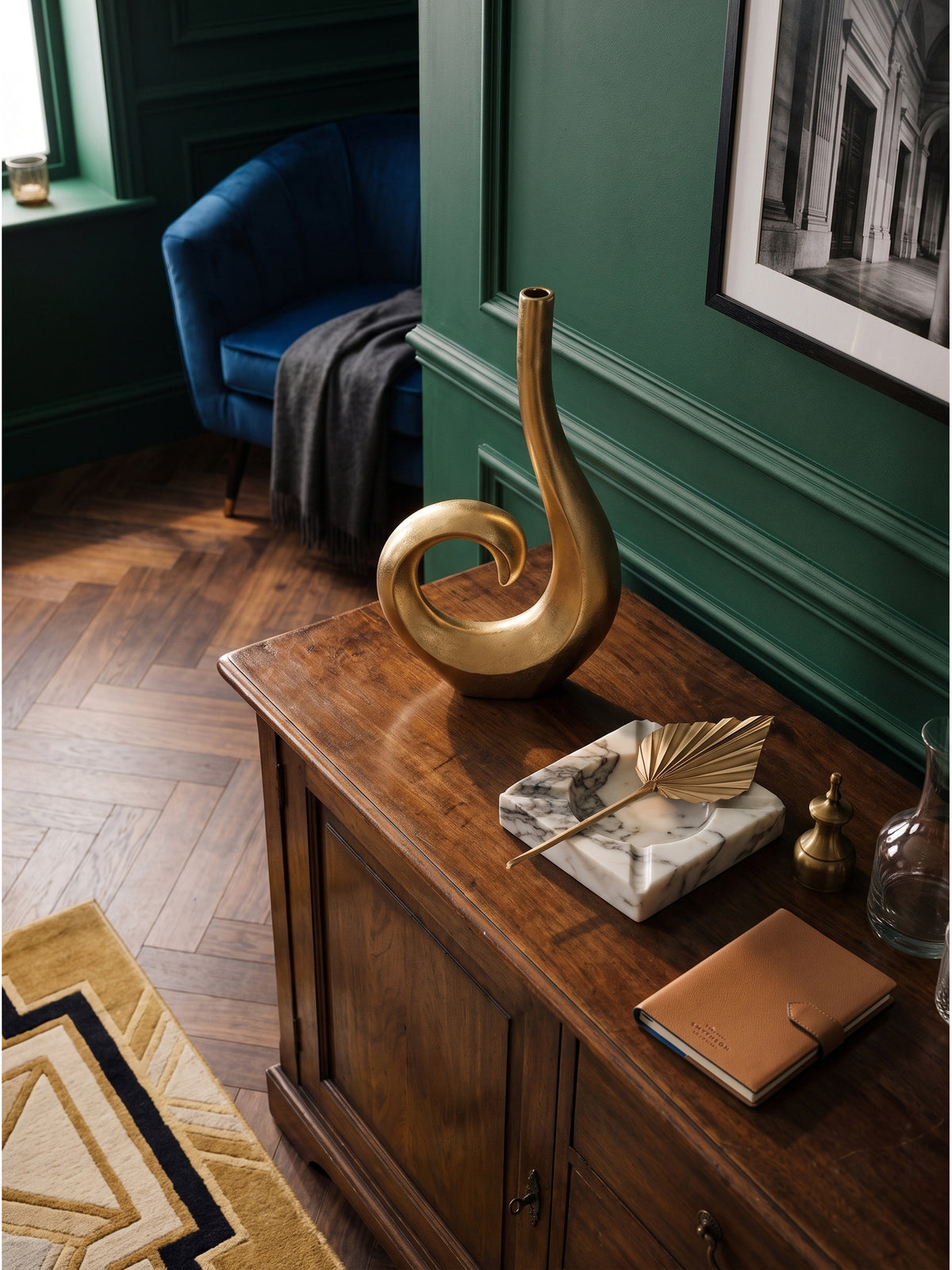 Draufsicht auf das klassische Wohnzimmer mit einer extravaganten Tischvase aus goldfarbenem Aluminium neben einem blauen Samtsessel._