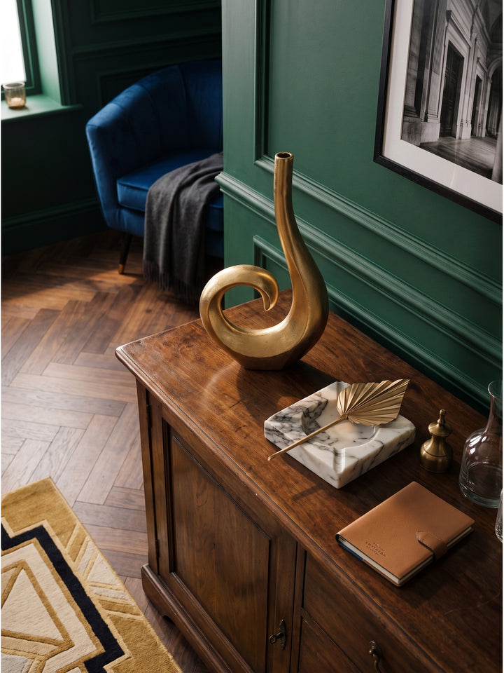 Draufsicht auf das klassische Wohnzimmer mit einer extravaganten Tischvase aus goldfarbenem Aluminium neben einem blauen Samtsessel._