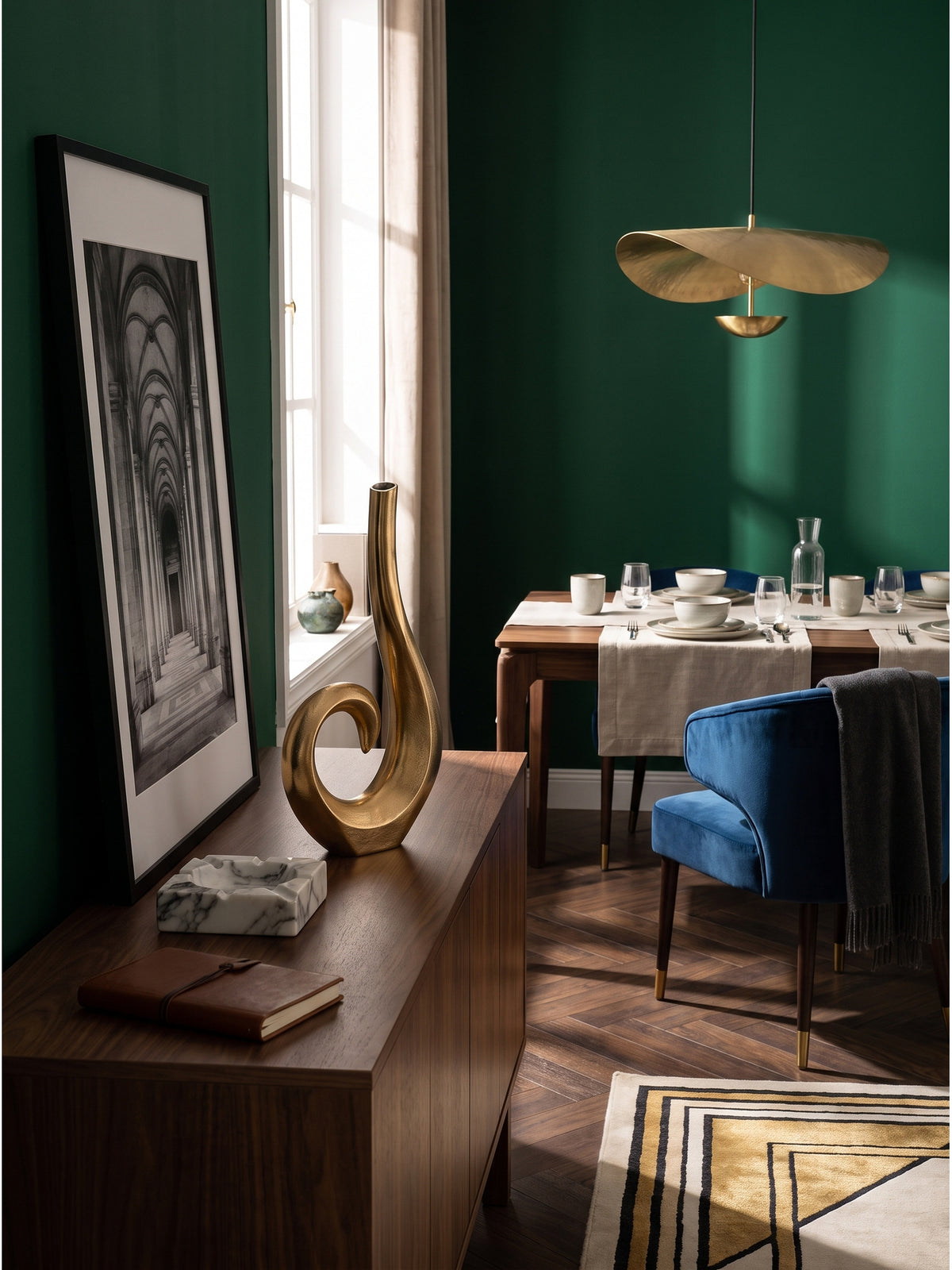 Zeitlose Tischdeko mit goldener Alu-Vase flankiert von patinierten Messing-Wandleuchten in einem luxuriös eingerichteten Raum._