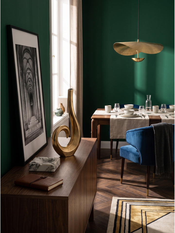 Zeitlose Tischdeko mit goldener Alu-Vase flankiert von patinierten Messing-Wandleuchten in einem luxuriös eingerichteten Raum._