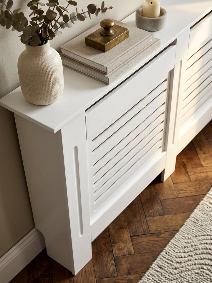 Detailaufnahme der matt weiß lackierten MDF-Oberfläche der Heizkörperabdeckung. Saubere Verarbeitung der horizontalen Holzlamellen und feine Kantenführung zeigen die hohe Qualität._