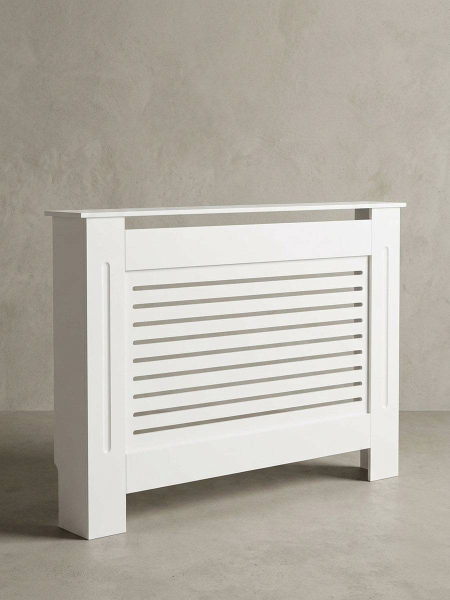 Freigestellte Frontansicht der weißen Heizkörperverkleidung. Die 112 cm breite Heizungsabdeckung besticht durch ihr klassisches Lamellen-Design und die matte Holzlackierung._