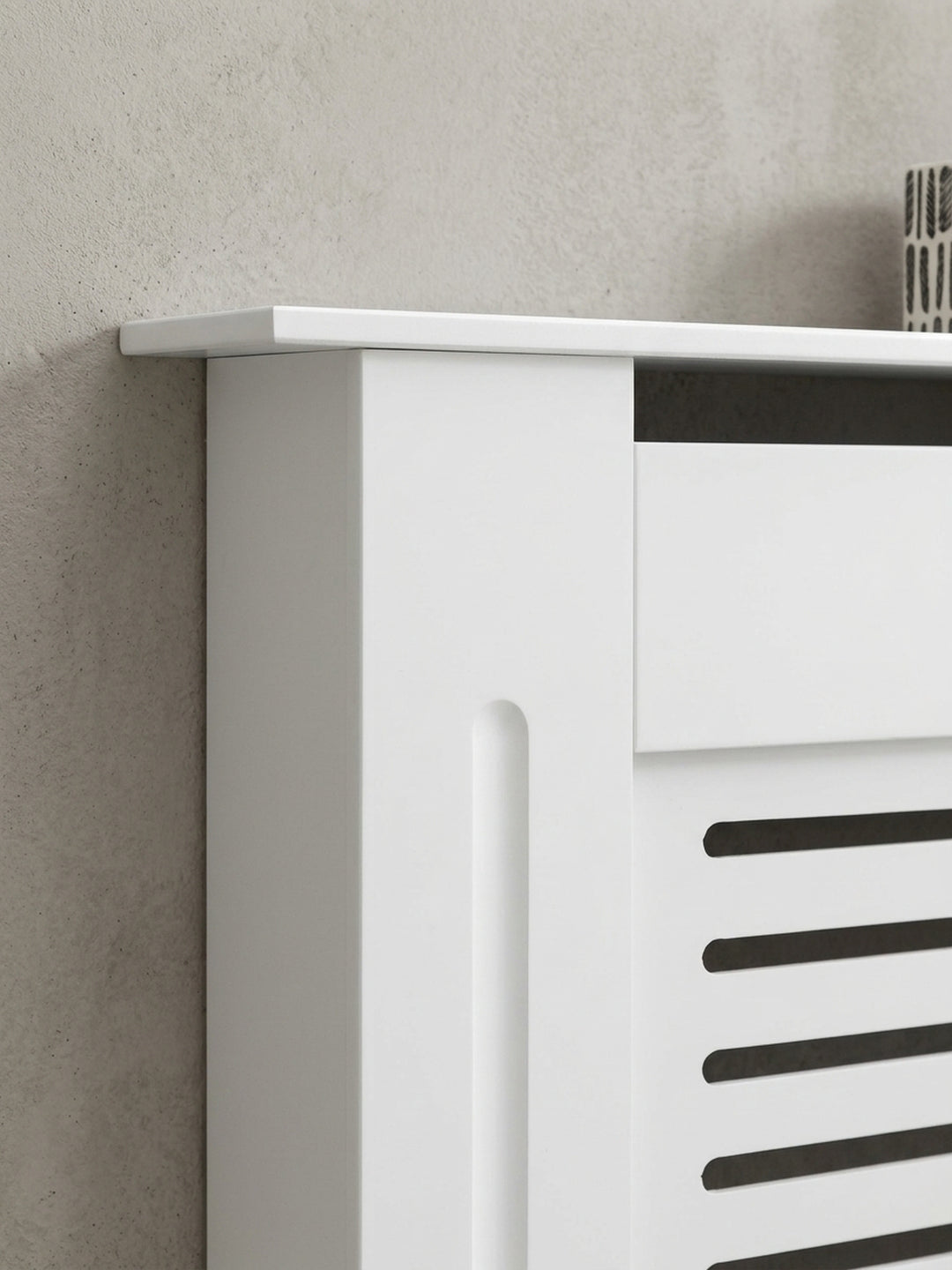 Kleine Heizkörperverkleidung aus MDF komplett in Weiß. Das geradlinige Design mit Lamellenfront verwandelt einen störenden Rippenheizkörper in ein praktisches Wandregal._