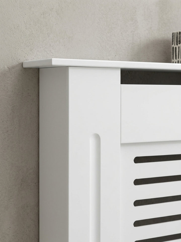 Kleine Heizkörperverkleidung aus MDF komplett in Weiß. Das geradlinige Design mit Lamellenfront verwandelt einen störenden Rippenheizkörper in ein praktisches Wandregal._