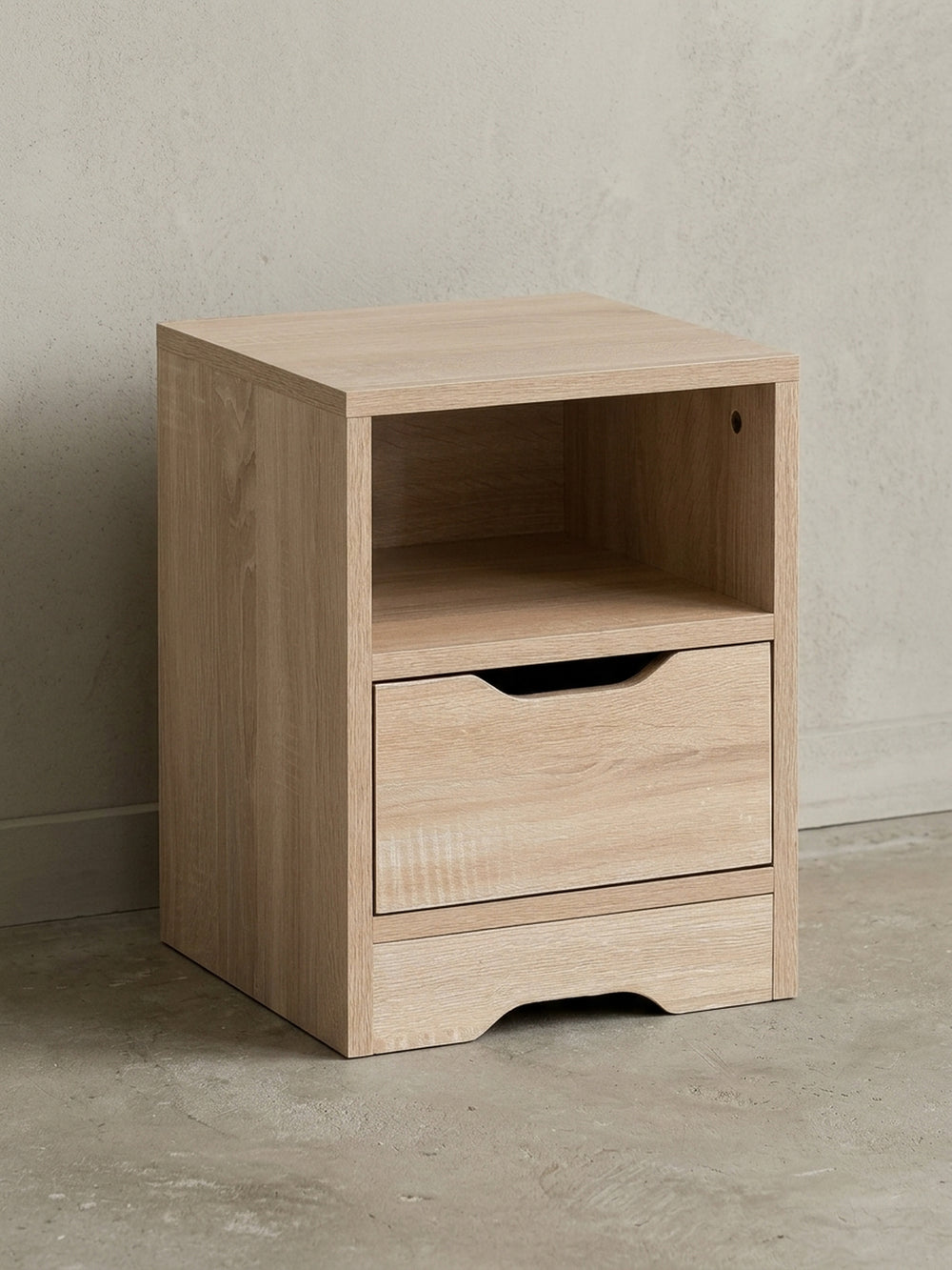 Schlichter Nachttisch in heller Sonoma Eiche von vorne. Das 43 cm niedrige Nachtschränkchen zeigt ein offenes Ablagefach und eine geräumige Schublade für idealen Stauraum direkt am Bett._