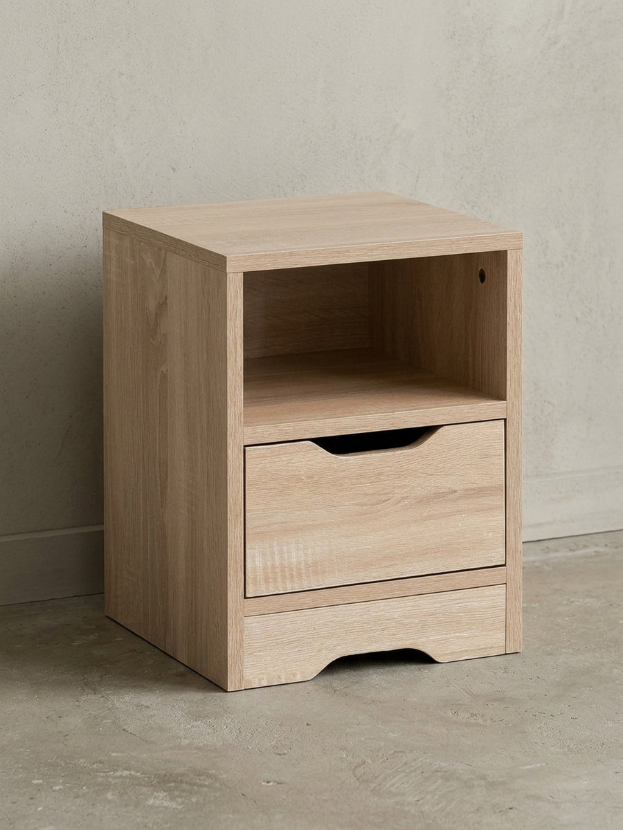 Schlichter Nachttisch in heller Sonoma Eiche von vorne. Das 43 cm niedrige Nachtschränkchen zeigt ein offenes Ablagefach und eine geräumige Schublade für idealen Stauraum direkt am Bett._