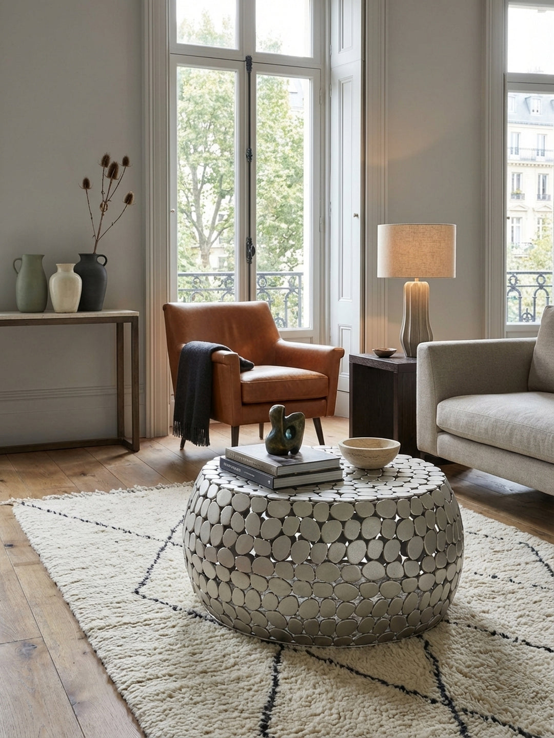 Moderner runder Couchtisch aus silbernem Aluminium im Wohnzimmer, stilvoll dekoriert auf einem beigen Teppich vor einem Sessel._