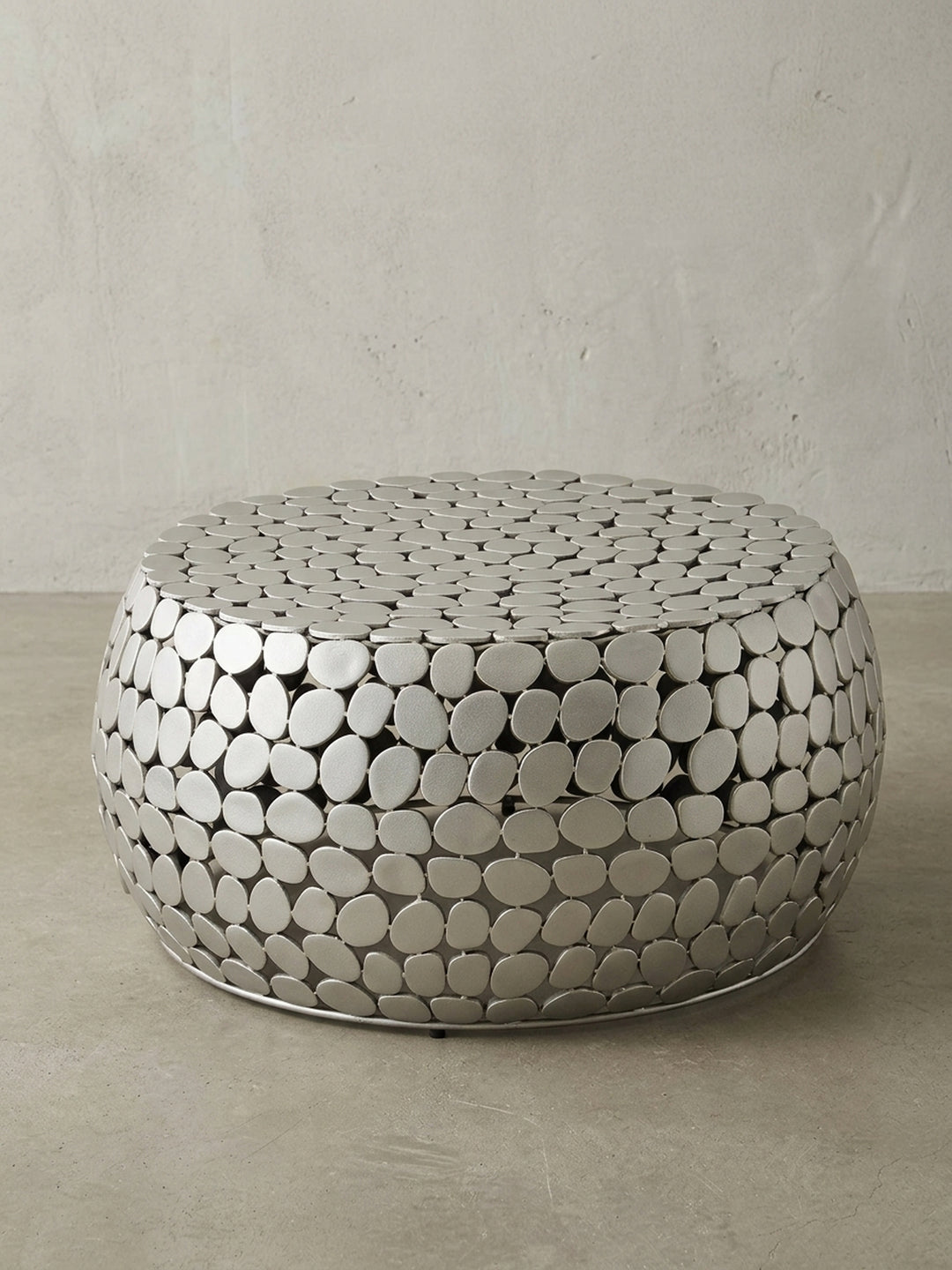 Freigestellter Couchtisch Metall Silber rund, zeigt die organische Kieselstein-Optik und die moderne Trommelform vor weißem Hintergrund._