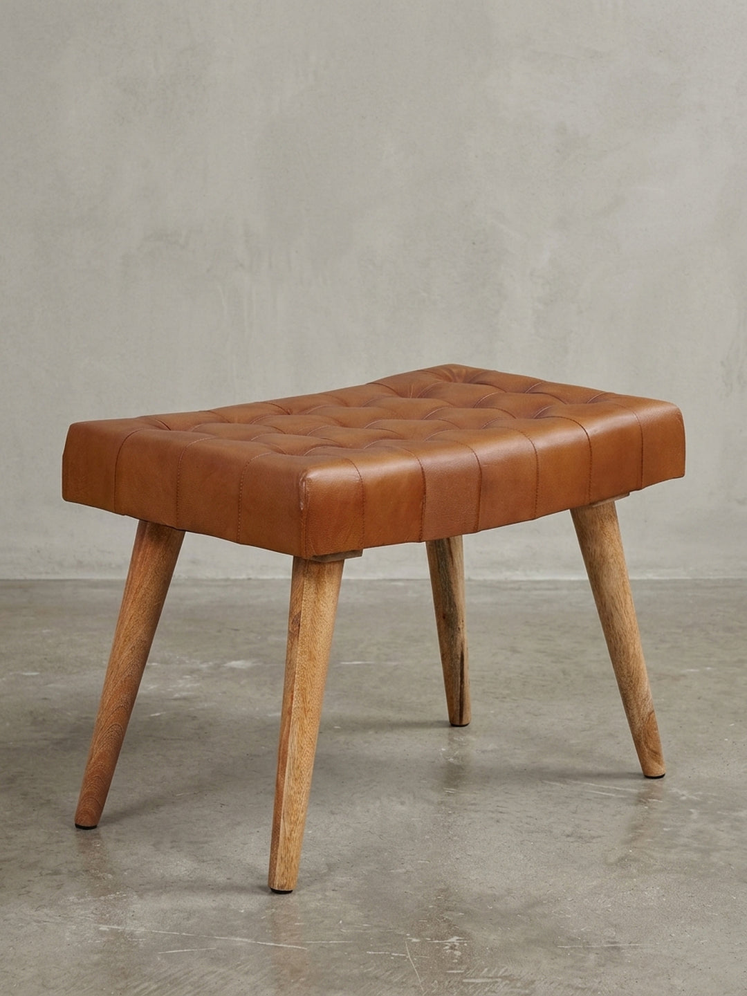 Freigestellter Sitzhocker mit braunem Echtleder-Bezug und Chesterfield-Steppung auf massivem Mangoholz-Gestell, Frontalansicht auf weißem Hintergrund._