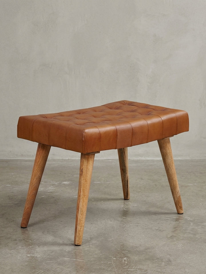 Freigestellter Sitzhocker mit braunem Echtleder-Bezug und Chesterfield-Steppung auf massivem Mangoholz-Gestell, Frontalansicht auf weißem Hintergrund._