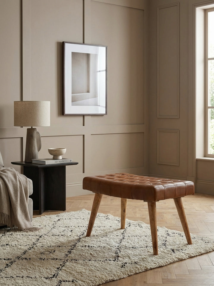 Eleganter Sitzhocker aus braunem Echtleder und Mango Massivholz im Chesterfield-Design, stilvoll in einem hellen Wohnzimmer mit Designer-Teppich platziert._