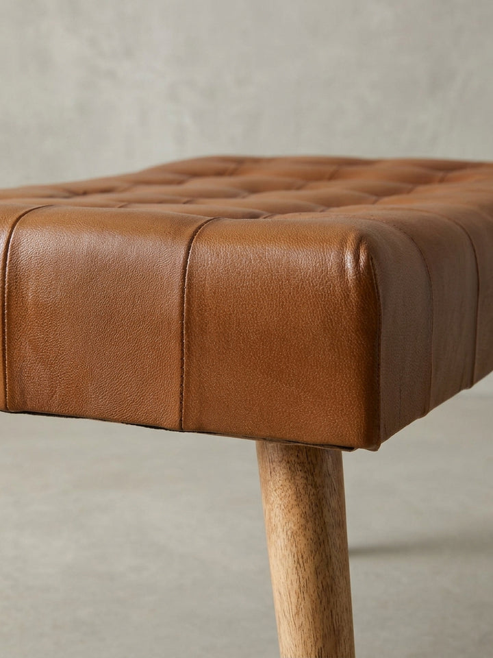 Detailaufnahme eines Knopfes der Chesterfield-Heftung des Hockers, umgeben von dem weichen, cognacfarbenen Echtleder der Sitzfläche aus Ziegenleder._