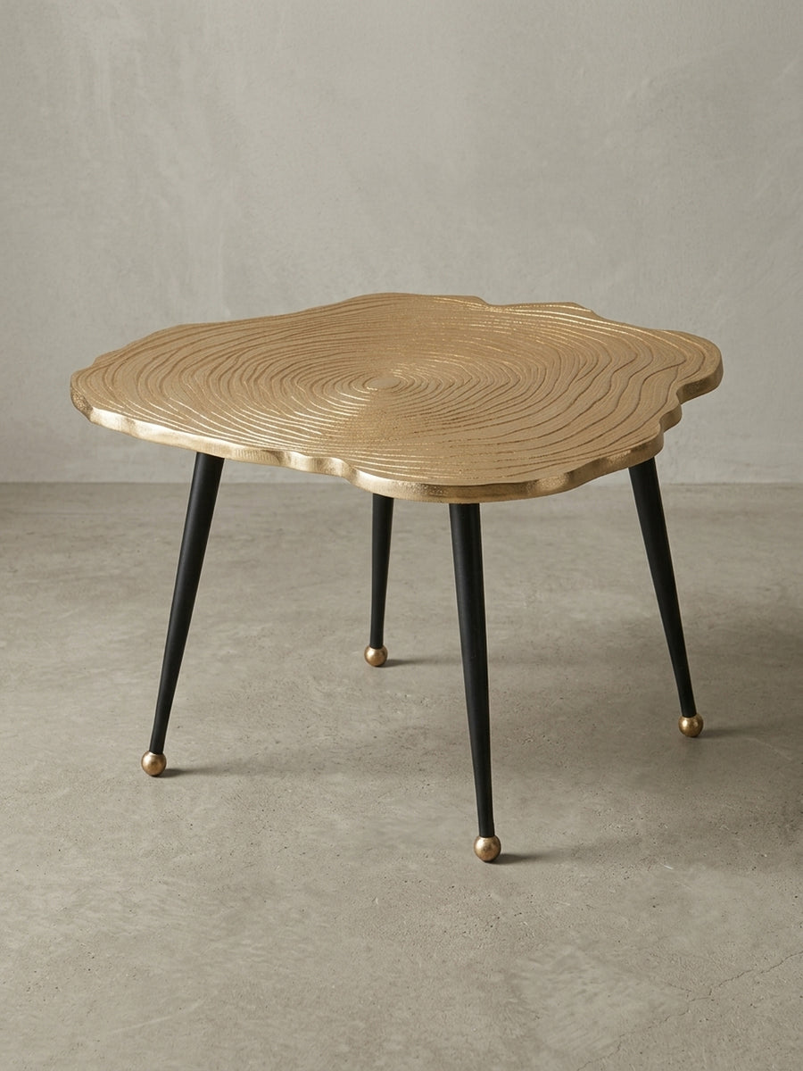 Gesamtansicht des modernen Anstelltischs, der die Materialkombination aus lackiertem Aluminium in Gold und Schwarz und seine skulpturale Wirkung zeigt._