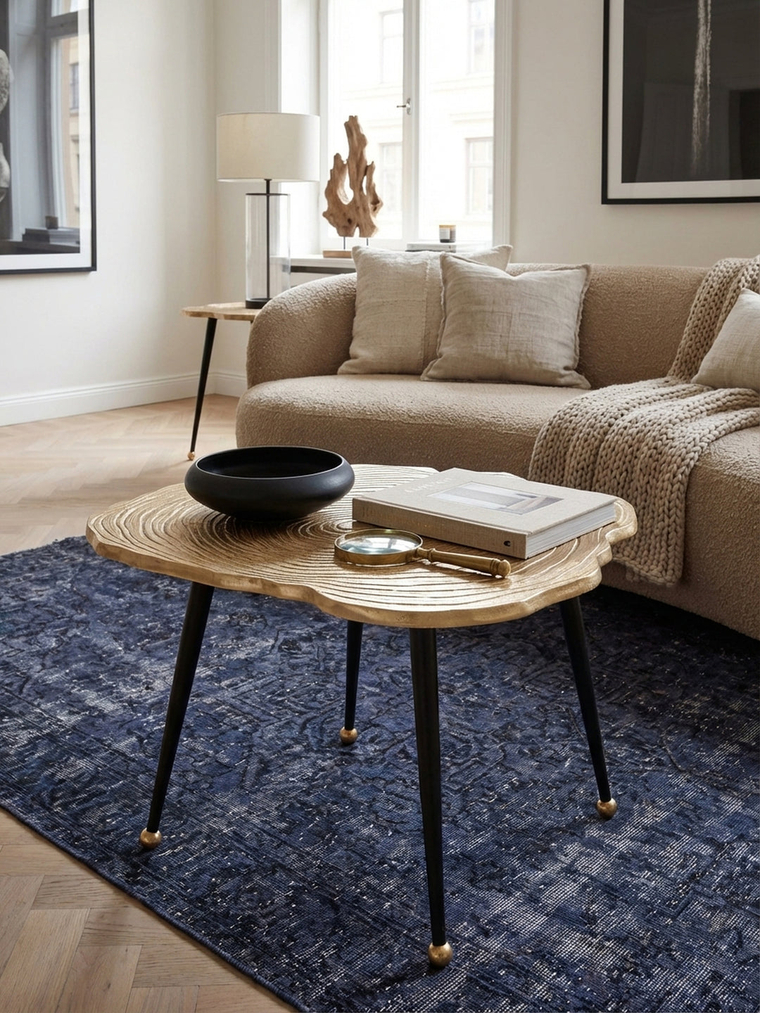 Eleganter Couchtisch in Gold mit Baumscheiben-Optik in einem stilvollen Wohnzimmer, platziert auf einem Designer-Teppich neben einem modernen Sofa._