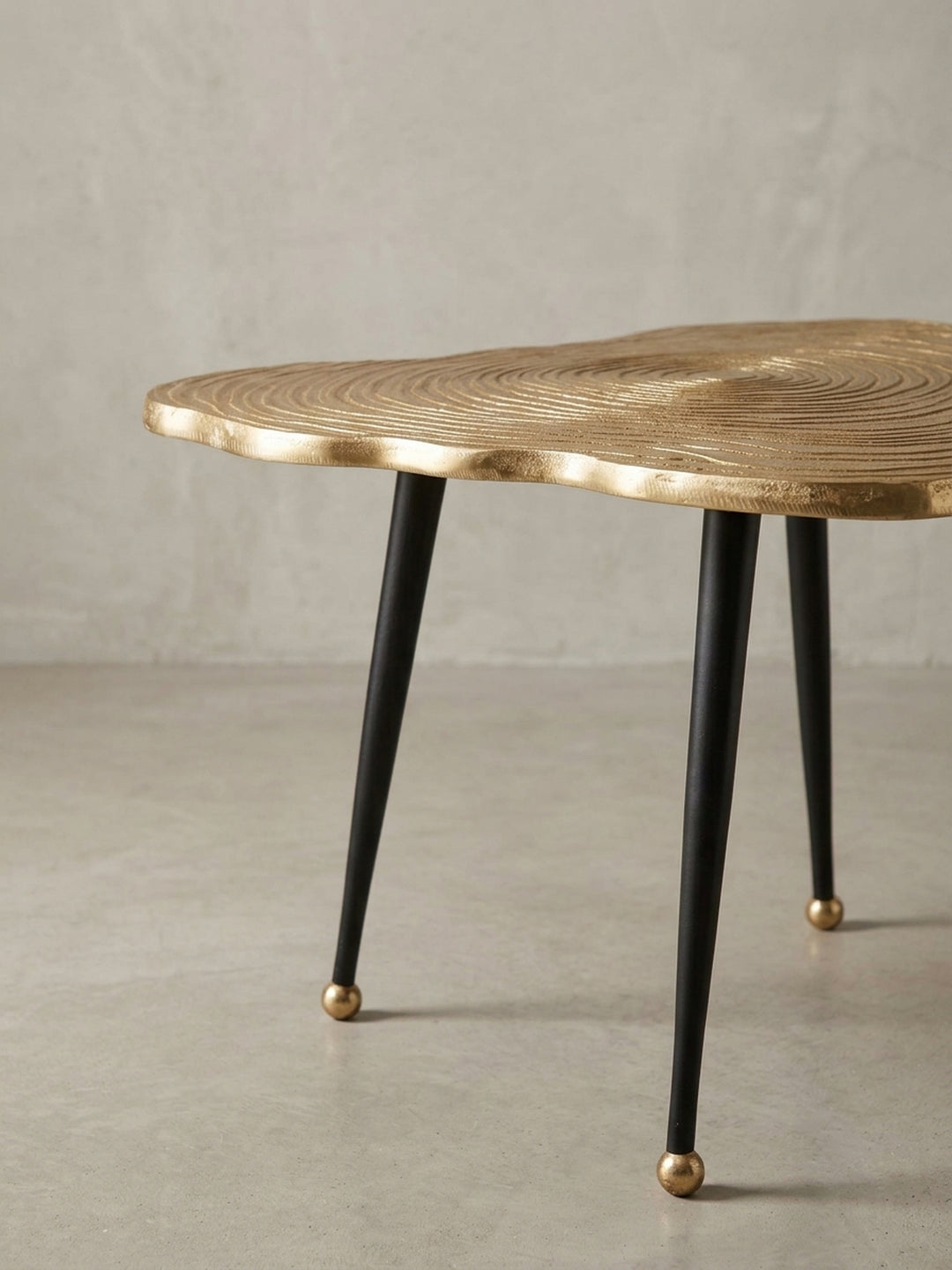 Nahaufnahme eines der schlanken, schwarzen Tischbeine mit dem dekorativen, kugelförmigen Fuß in Gold, ein Detail des modernen Kaffeetisch-Designs._