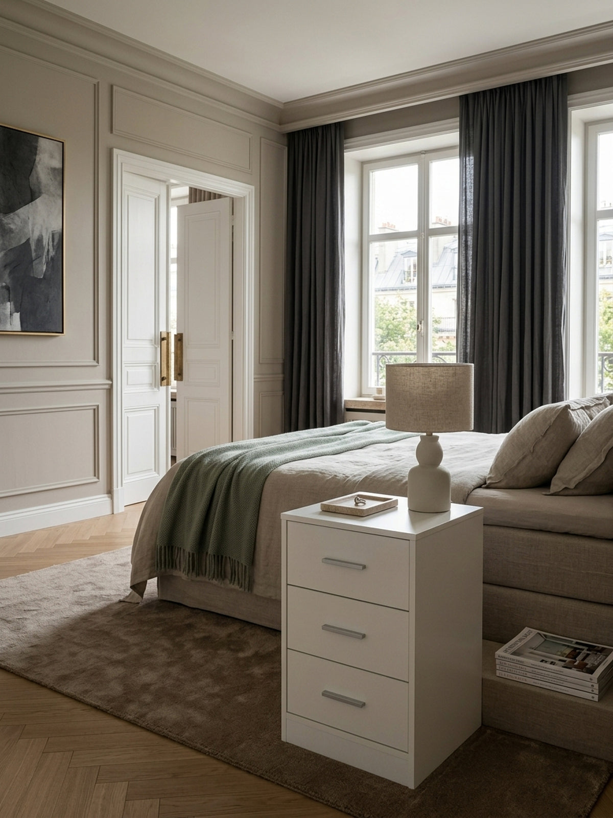 Moderner weißer Nachttisch mit 3 Schubladen im eleganten Schlafzimmer. Die 68 cm hohe Nachtkonsole steht perfekt neben einem luxuriösen Boxspringbett mit Leinenbezug._