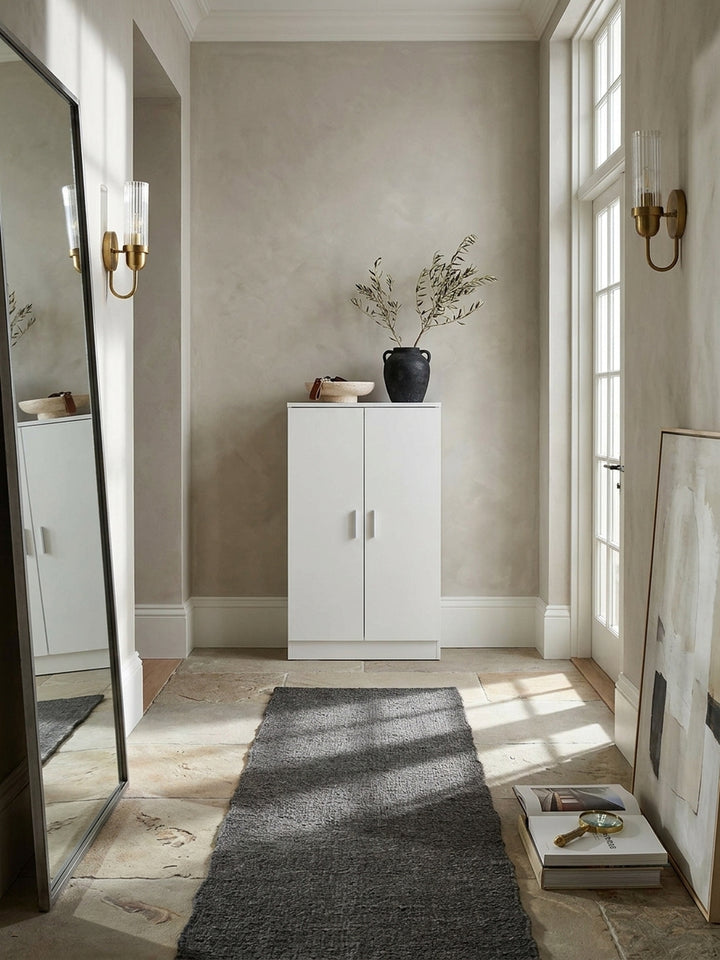 Schlichter Schuhschrank Weiß 55x108x35 cm in einem stilvollen Eingangsbereich auf Kalksteinboden neben einem minimalistischen Spiegel positioniert_