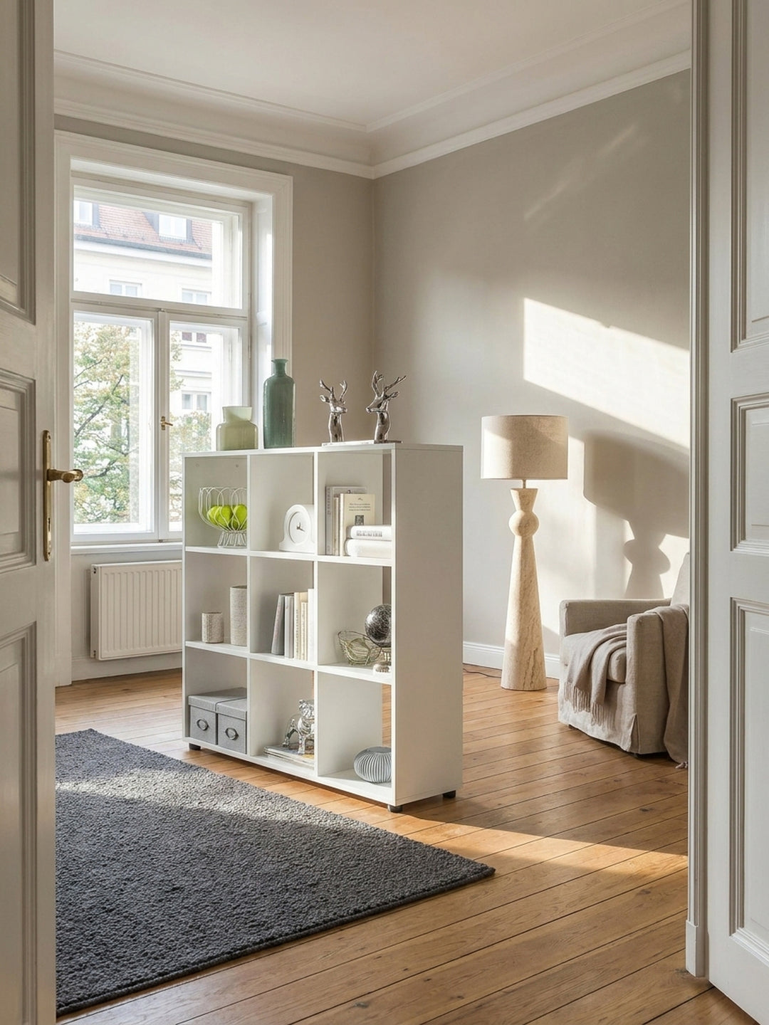 Modernes Bücherregal aus weiß lackiertem Holz mit 9 Fächern 108x104x29 cm als eleganter Raumteiler in einem lichtdurchfluteten minimalistischen Wohnzimmer mit Eichendielen._