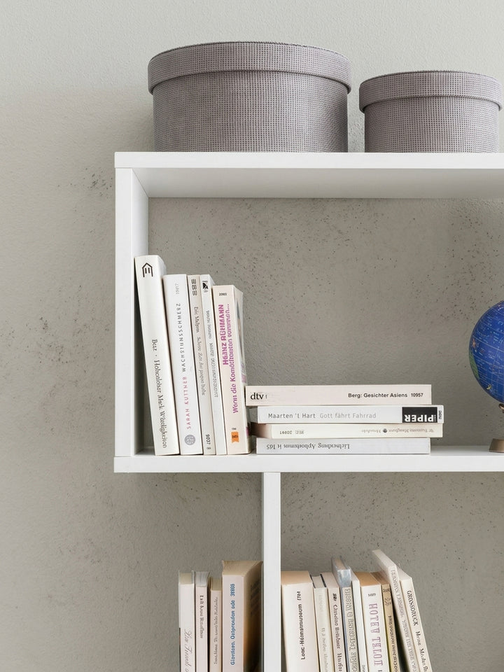 Gesamtübersicht des modernen weißen Zick-Zack-Regals. Das schlichte Design des freistehenden Raumtrenners fügt sich nahtlos in minimalistische oder skandinavische Raumkonzepte ein._