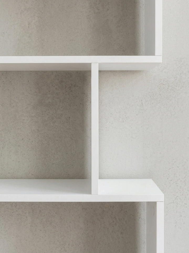 Detailansicht der Rückseite des freistehenden Raumtrenners. Die unsichtbaren Verbindungen der weißen Spanplatten betonen das minimalistische Zick-Zack-Design des modernen Bücherregals._