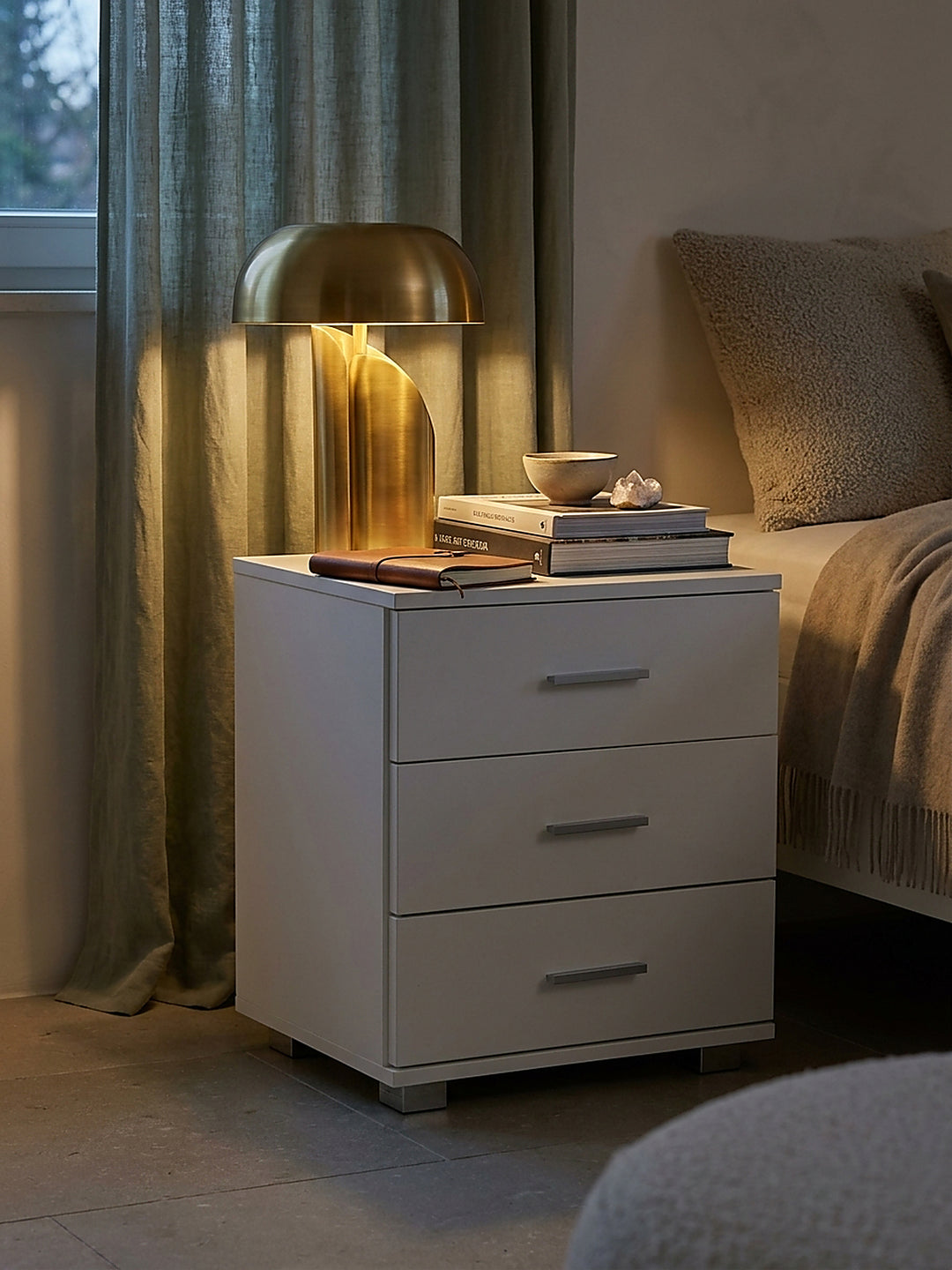 Styling-Arrangement auf einem puristischen weißen Nachttisch mit einer handgetöpferten Keramikschale und einem ledergebundenen Buch._