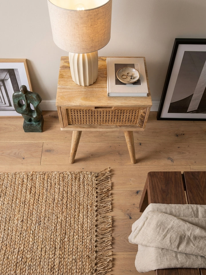 Draufsicht auf die Nachtkonsole aus Mangoholz mit Rattan-Schublade, perfekt arrangiert auf einem Jute-Teppich neben dem Bett für eine harmonische Schlafzimmer-Gestaltung._