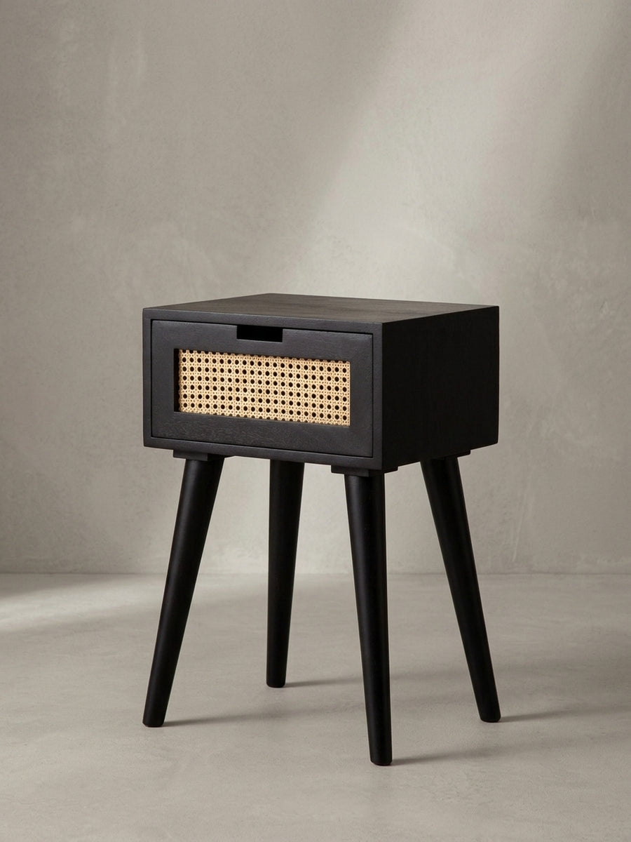 Schwarzer Nachttisch in der 3/4-Ansicht von links, die Tiefe des Korpus und die elegante Form der konischen Holzbeine betonend._