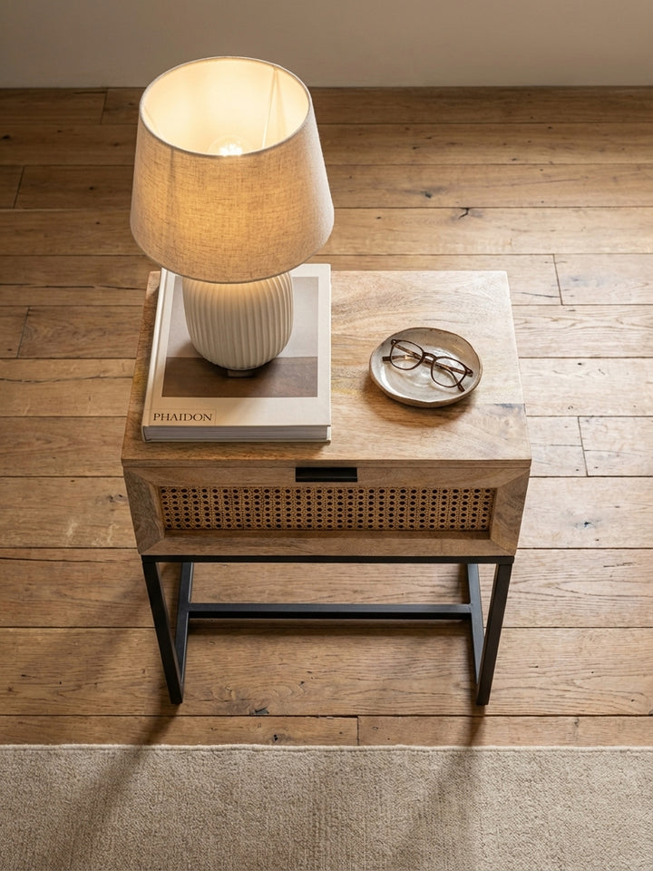 Draufsicht auf den Nachttisch aus Mangoholz neben einem Bett, platziert auf einem beigen Wollteppich mit Holzdielenboden._
