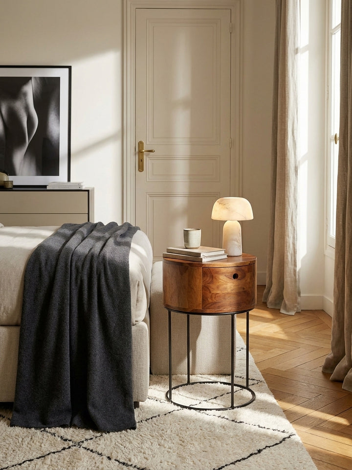 Runder Nachttisch aus Sheesham Massivholz neben einem Leinenbett in einem hellen, minimalistisch eingerichteten Schlafzimmer mit Holzboden._