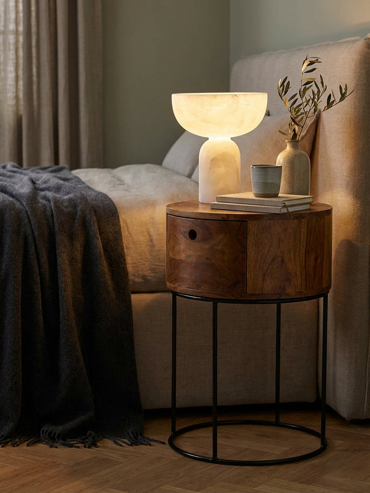 Styling-Detail: Ein offenes Buch liegt auf dem runden Sheesham-Nachttisch, dessen Schublade leicht geöffnet ist und einen gemütlichen Moment am Bett zeigt._