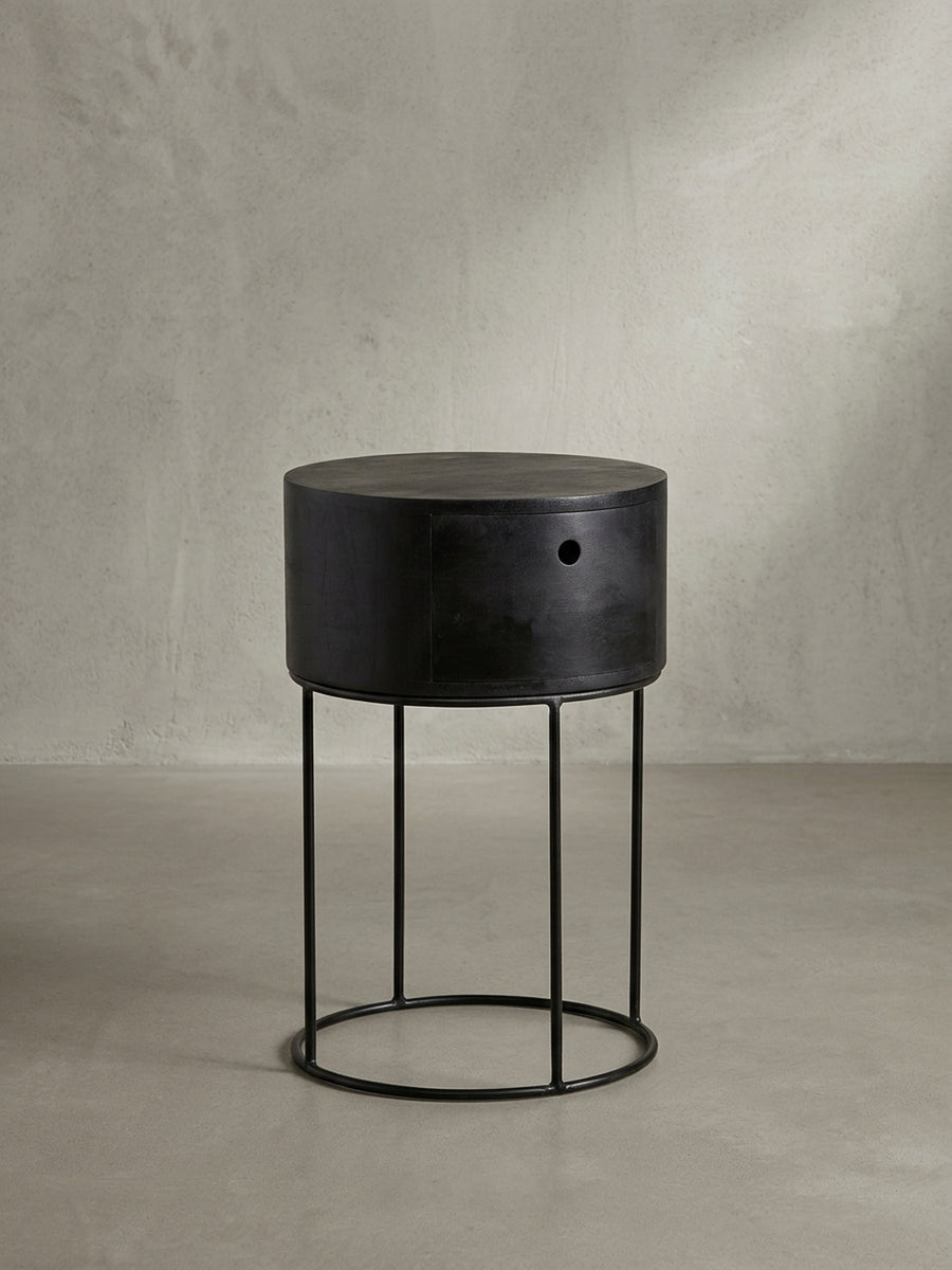 Seitenprofil des schwarzen Nachttisches, das das ausgewogene Verhältnis zwischen dem soliden Holzzylinder und dem leichten, luftigen Metallgestell zeigt._