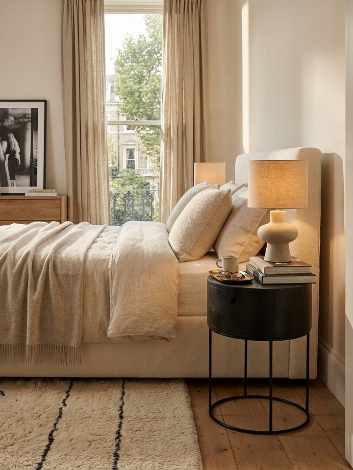 Der schwarze Mango-Nachttisch im Zusammenspiel mit einem Bett mit hohem Stoffkopfteil und einem flauschigen Wollteppich, als Inspiration für ein modernes Schlafzimmer._