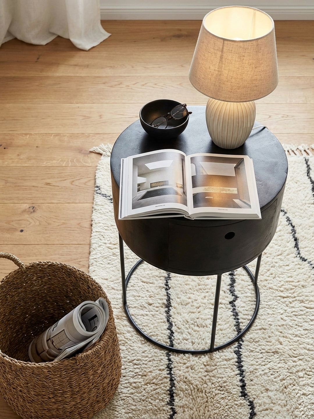 Draufsicht auf den schwarzen Design-Nachttisch mit Schublade, harmonisch arrangiert auf einem Beni Mrirt Teppich neben dem Bett und einer modernen Tischleuchte._