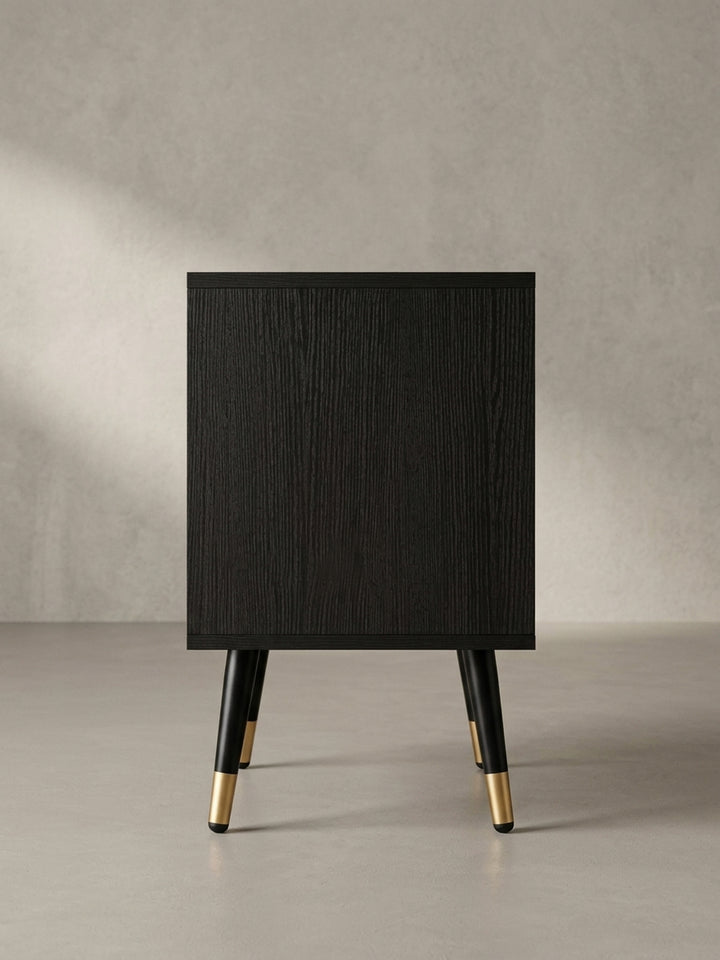 Nahaufnahme des minimalistischen, goldfarbenen Griffs an der geriffelten Schubladenfront des schwarzen Design-Nachttisches._