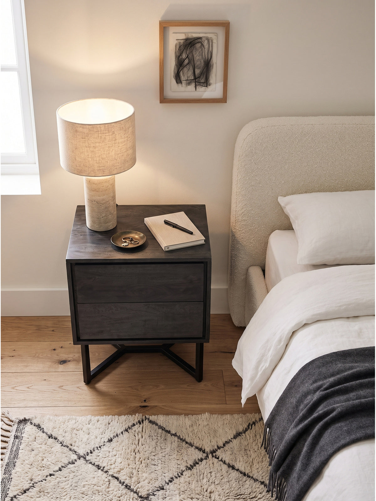 Draufsicht auf die schwarze Nachtkonsole mit Metallgestell auf warmem Eichenparkett neben einem Boxspringbett im modernen Design._