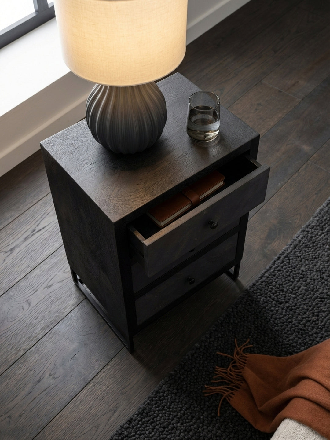 Draufsicht auf einen Design-Nachttisch mit drei Schubladen neben einem Boxspringbett, der die klare Anordnung im urbanen Schlafzimmer zeigt._