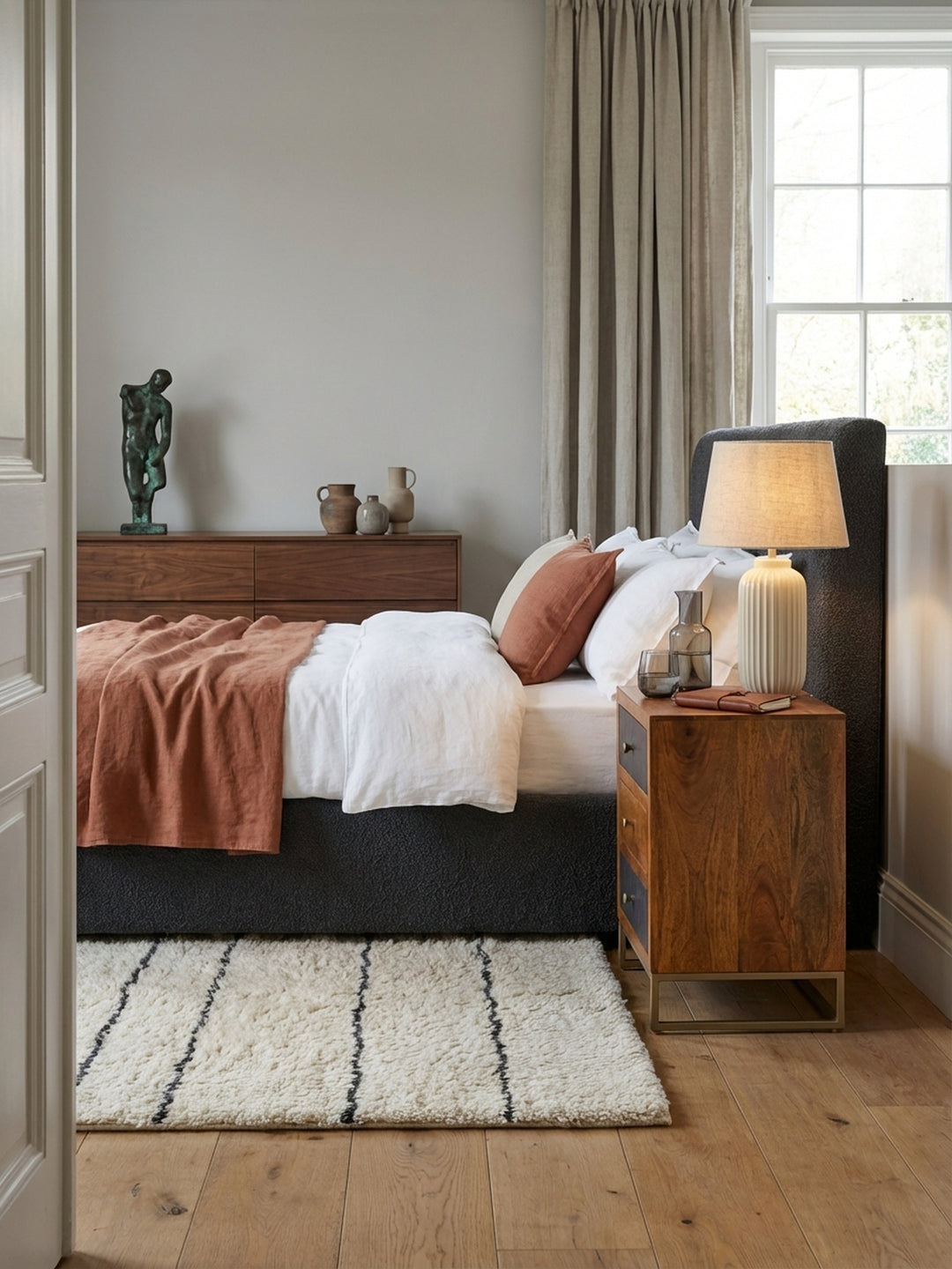 Moderner Nachttisch aus Mango Massivholz und grauer Steinoptik neben einem Boxspringbett in einem hellen, minimalistisch eingerichteten Schlafzimmer mit Holzboden._